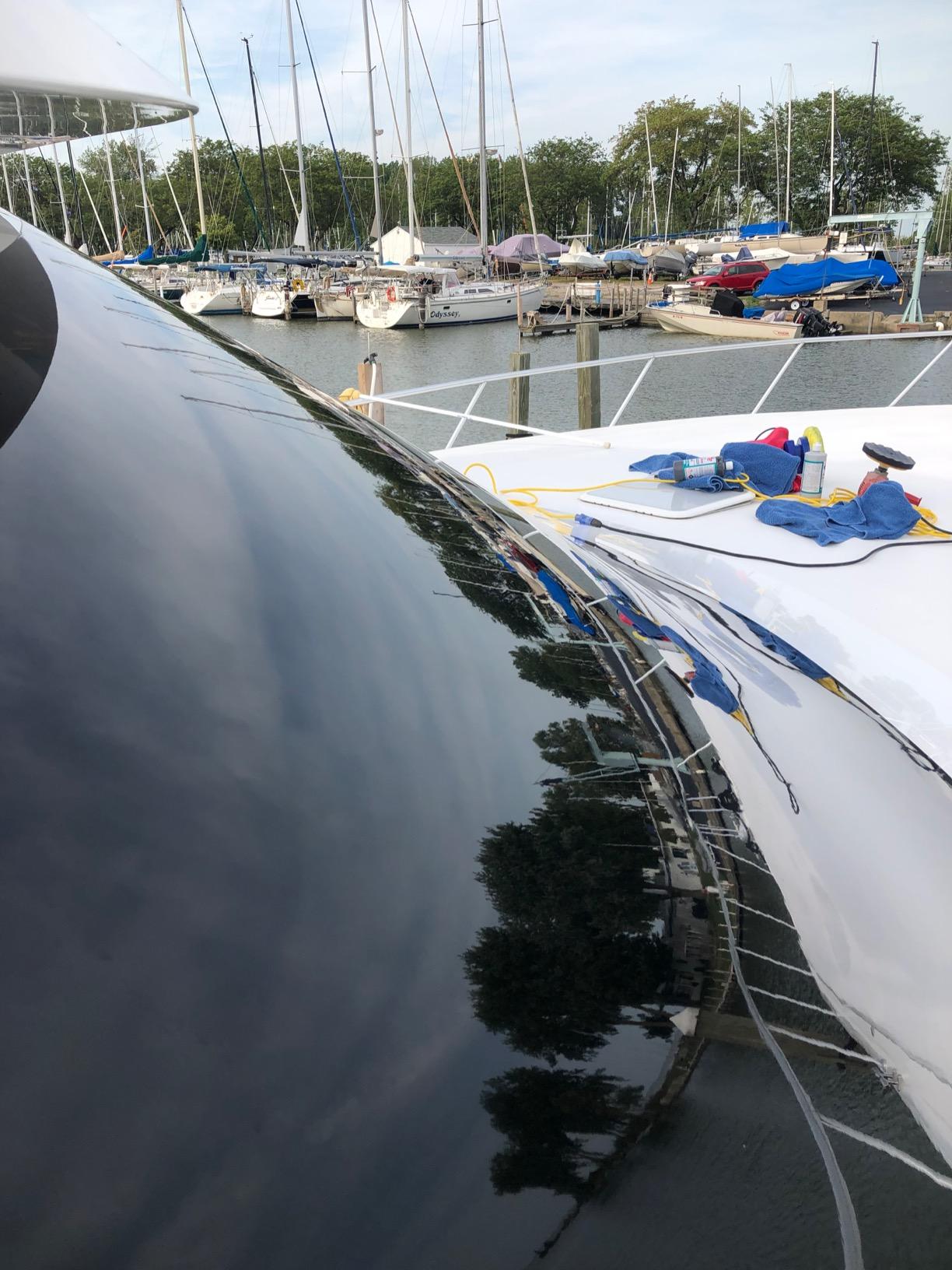 Boat in a marina with a glossy, restored finish after paint correction, reflecting in the water with other boats visible in the background.