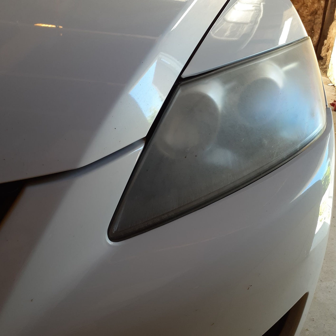 Close-up of a cloudy headlight showing oxidation and fading, typical of vehicle headlights before restoration.