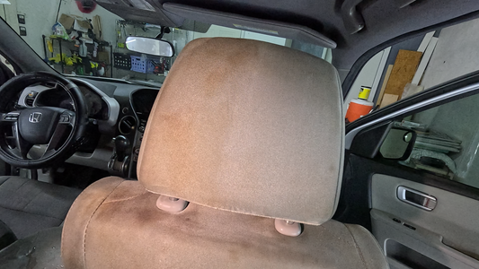 Headrest of a vehicle undergoing our Interior Revival Package. A striking half-and-half view shows dirty staining on one side and clean, refreshed fabric on the other.