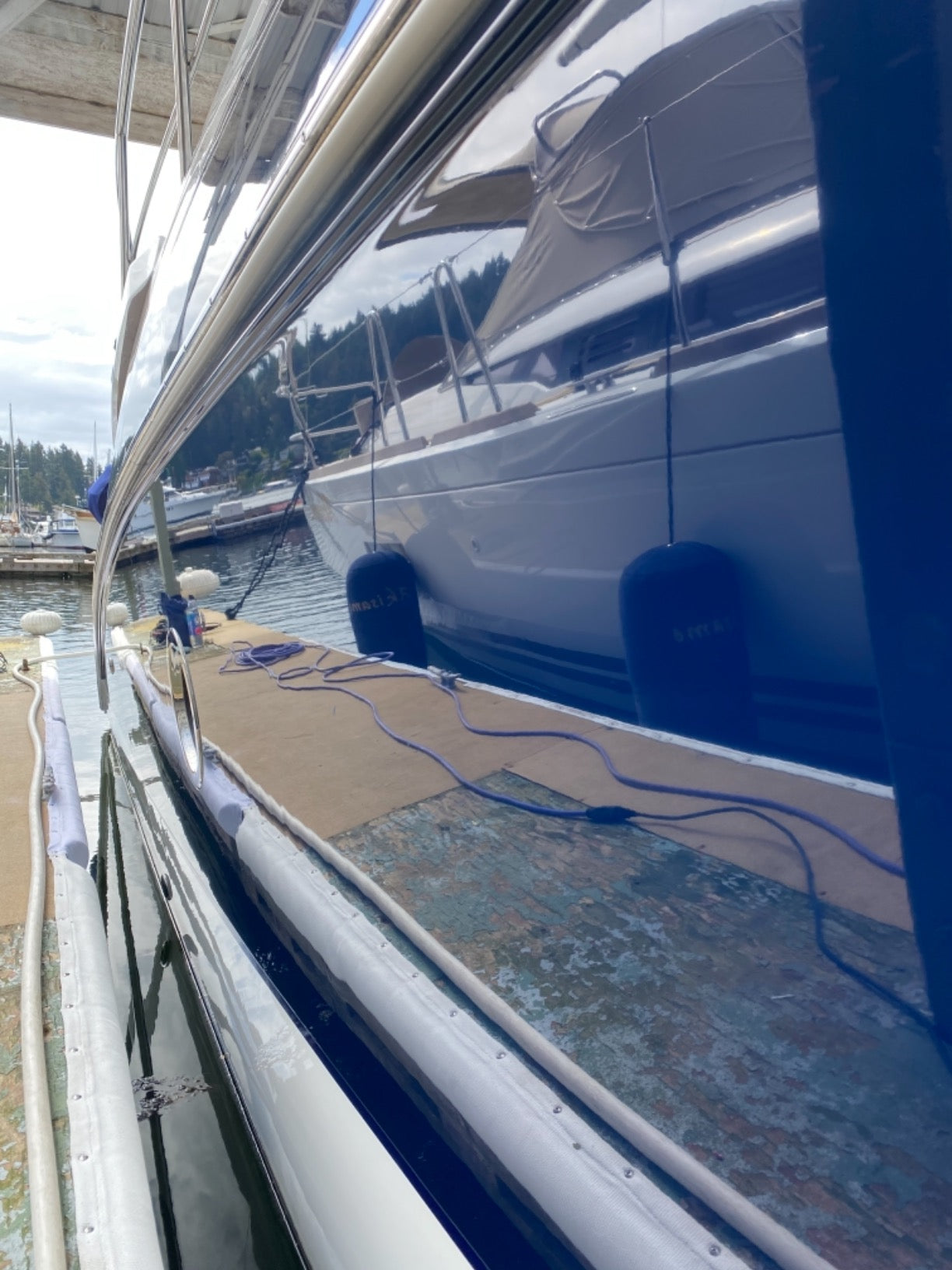 Yacht hull after paint correction, removing oxidation and revealing a glossy, flawless finish with a clear reflection.
