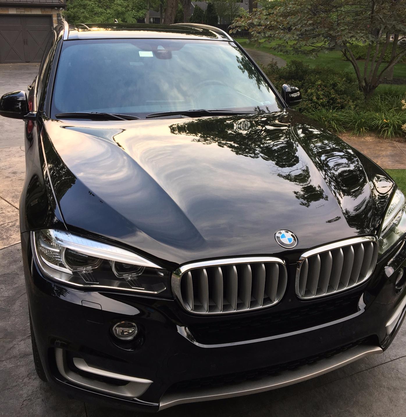 A BMW after our two-stage paint correction and graphene ceramic coating job, with the clouds reflected off the hood.
