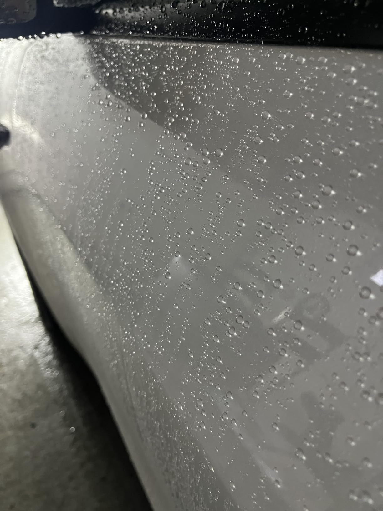 Detailed shot of water beading on a white car, highlighting the hydrophobic properties of graphene ceramic coating