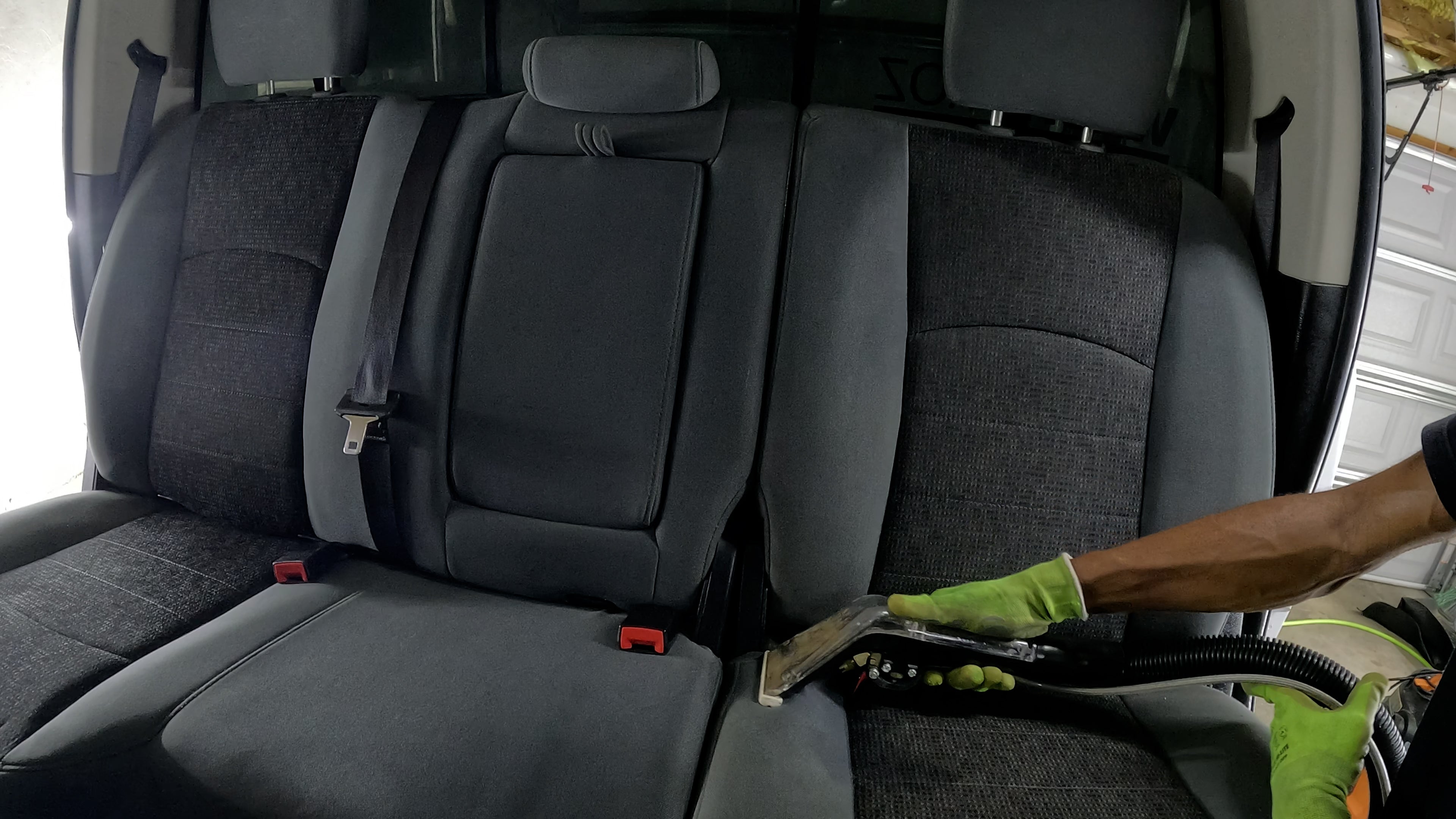 Detailer's arm operating an extraction machine, effectively pulling out dirt from a dirty vehicle interior during a deep cleaning process.