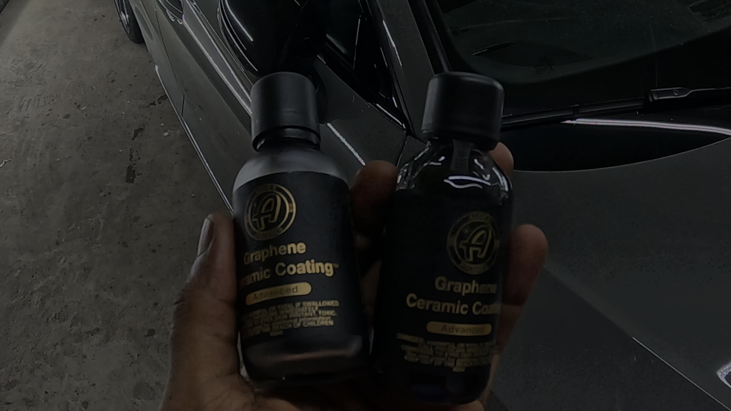 Detailer holding two bottles of graphene ceramic coating at Finishline Detailing Garage LLC in Tallahassee, FL, showcasing premium protective products for automotive finishes.