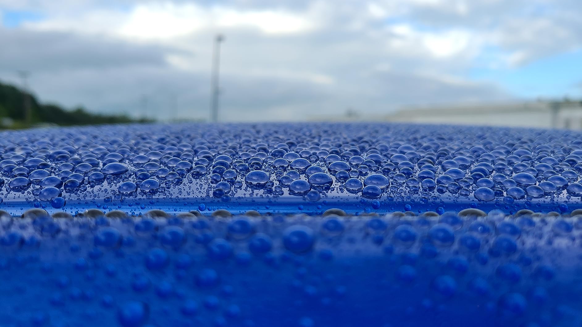 Macro shot of water beading on a blue vehicle surface treated with graphene ceramic coating.