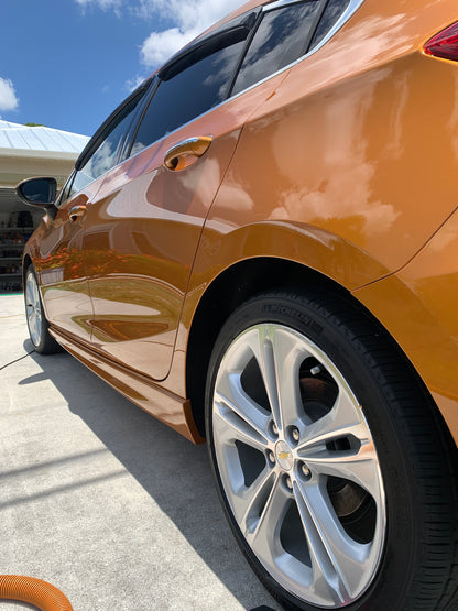 Low rear view of the orange Chevy, showing the side with the client's house reflecting off the car after our paint enhancement.
