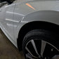 Low-angle shot from the wheel, showcasing the white car from a unique perspective, highlighting its glossy finish after paint correction and graphene ceramic coating.