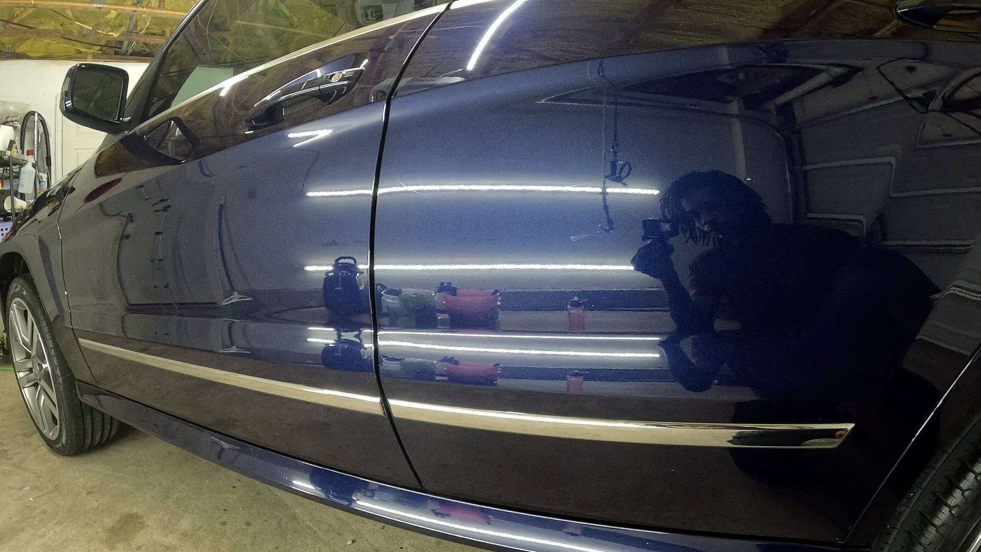 Left side of the blue Mercedes, reflecting me, the shop, and detailing tools, after a two-step paint correction that restored the glossy finish