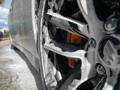 Low-angle shot from the wheel, capturing the foam bath in action as it begins the pre-wash process for a clean, shiny finish.