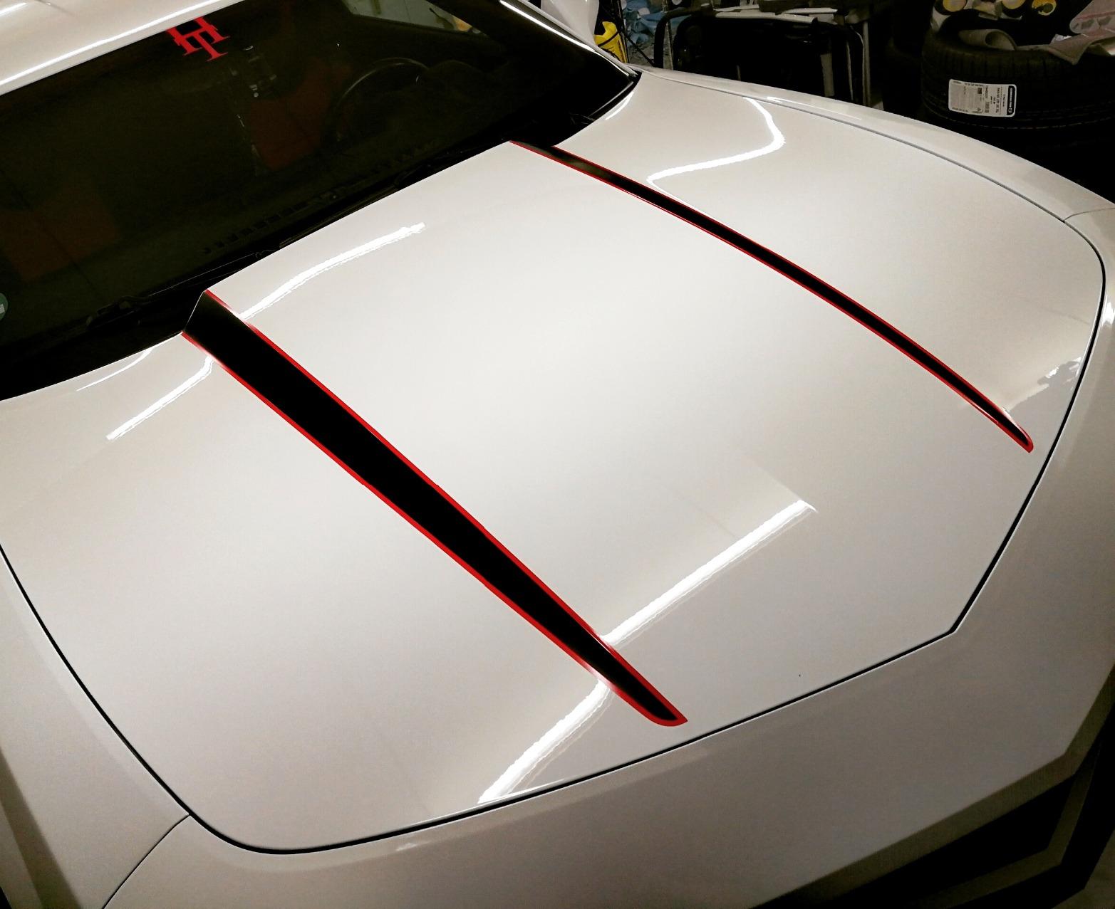 White Camaro hood after a paint enhancement, showcasing a glossy and reflective finish.